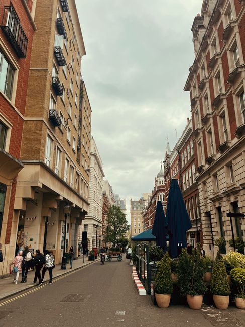 A black and white photograph of a narrow city street in Soho, London, showing a row of parked cars lining both sides of the road, with some vehicles partially visible due to the dense arrangement. In